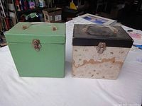 Two closed vintage 45 record cases, one green and one beige with black top, placed side by side to show external condition and design.