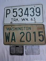 Photo showing both Washington license plates and two automobile fender tags from Nissan and Chevrolet laid out on fabric.