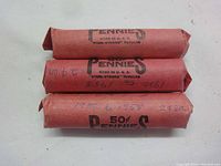 Three red paper rolls of Lincoln wheat pennies with handwritten years and denomination markings on wrapping.