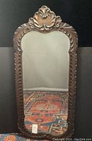 Full view of antique wall mirror showing ornate carved wooden frame and beveled edged mirror glass.
