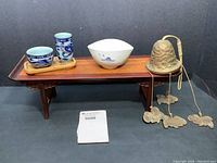 Full lot showing rosewood altar table holding two blue-and-white mini porcelain cups on a wooden tray, one larger white porcelain tea cup, and vintage brass wind chime with Foo Dog-shaped chimes