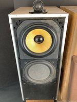 Front view of one speaker showing yellow Kevlar midrange cone above a dusty foam surround woofer, tweeter visible but missing grill.