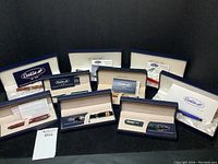 Front view of nine Conklin pen boxes displayed on black background