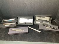 Various Lamy fountain and ball pens with boxes displayed on black surface.