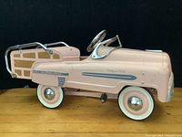 Side view of pink woody station wagon pedal car showing original paint and wood panel decals, whitewall tires with chrome hubcaps.