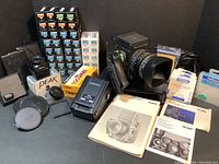 Overview of camera body, lens, film boxes, charger, manuals and accessories on black background