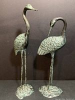 Pair of patinaed brass crane sculptures with detailed feather engraving, one with neck straight and other with neck curved downward.