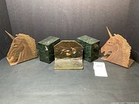 Five vintage bookends shown together: two brass unicorn heads, two green marble cubes, and one spelter bookend with a painting relief.