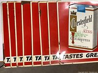 Eight identical rectangular tin advertising signs for Chesterfield King Cigarettes, red background with white border and 'Tastes Great' slogan.