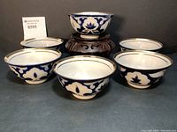 Set of six royal blue and gold hand painted porcelain tea cups arranged in a semi-circle with one on a wooden stand.