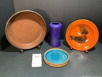 Lot overview showing four pottery pieces: brown plate, blue vase, orange plate, turquoise plate