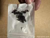 Clear plastic bag with 16 matte black stud earrings with butterfly backs held by fingers.