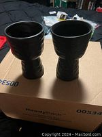 Two black ceramic planters or vases standing upright on a cardboard box, showing the textured exterior and wide opening.