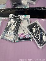 Photo of three different new cell phone cases in original plastic packaging, showing a black case labeled 'FASHION CASE', a floral design case, and another black case labeled 'STYLE POUR'.