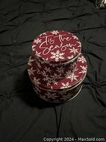Two round Christmas cookie tins stacked, decorated with white snowflakes on red, large tin lid says 'Tis the Season'