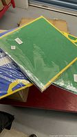 Photo of three felt boards stacked with visible green, blue, and yellow felt surfaces and yellow edges, still in clear plastic wrapping.