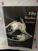 Softcover book Fifty Shades Darker by E L James showing front cover with masquerade mask image.