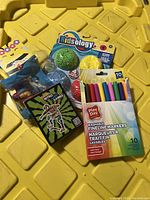 Photo showing a bundle of new kid's items including Play Day fineline markers, Nitrot Games cards, and Kidsology textured balls on a yellow surface.