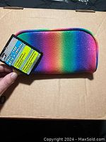 Photo of the pencil case held against a brown cardboard background showing the rainbow gradient fabric and attached tags indicating new condition.