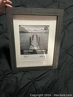 Dark brown wood finish 11x14 photo frame held upright on black tufted background. Frame has a white mat and includes placeholder photo of pier and lake.