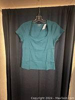 Teal Old Navy women's square neck T-shirt hanging on a hanger with new tags attached, shown against a dark curtain backdrop.