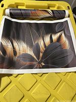 Rolled non-framed abstract leaf wall art print showing metallic gold and dark gray detailed leaves on black background.
