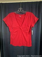 Red women's t-shirt displayed on a hanger against a dark blue curtain background showing short sleeves and twist front design.