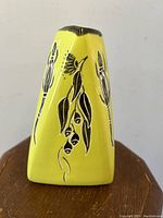 Front view of yellow pyramid pottery vase with black floral designs
