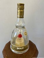 Front view of clear glass Bols Ballerina liquor bottle with gold screw cap and small ballerina inside wearing a red dress.