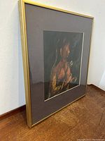 Angled side view of framed painting showing gold frame and brown surface underneath