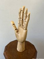 Frontal view of the jointed wooden figural hand with fingers positioned upright on wooden platform.