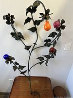Overall view of wrought metal floral wall light with five colorful bulbs attached, displayed against wall and table for scale.