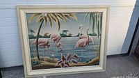 Frontal view of framed airbrushed canvas showcasing five pink flamingos in tropical lakeside scene.