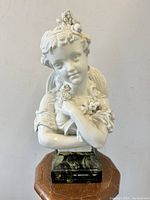 Front view of the white glazed porcelain angelic lady bust on bronzed metal base, showing details of face and flowers.