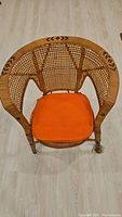 Top view of the antique wicker chair showing the lattice woven back and orange cushion.