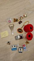 Overview of collector pins, money clip, keychain, bottle opener and poppy pins displayed on wooden surface