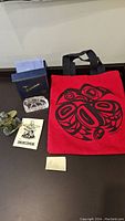 Lot items on display: jade Inukshuk sculpture, clear crystal colt carving, red tote bag with native art, and original boxes and card.