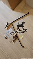 Iron Welcome sign with horse silhouette, two keychains, zipper charms, and wooden horse decoration arranged on floor for lot display