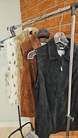 Photo of three ladies' vests hanging on a rack, showing black suede, brown suede, and white with black spots faux fur vest.