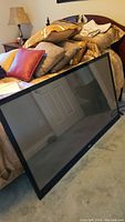 Flat screen plasma television leaning against bed, showing front screen and black bezel with LG branding.