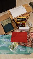 Cloth napkins and placemats in green, beige, and red colors, dolphin shower curtain with dolphin pattern and fish clips, box of vacuum cleaner bags, and other small items packed in boxes.