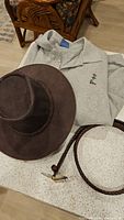 Photo showing brown leather folding hat, woven leather belt coiled, and gray sweatshirt on table