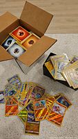 Top view of a box with various Pokemon Energy cards and some laminated Pokemon cards spread on the ground.
