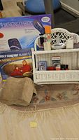 Full lot showing massaging cushion box, comfort blanket, leg pillow on floral rug, white wicker wall shelf with boxed soaps and beauty items.