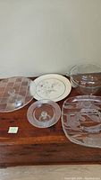 Overview of ceramic plate, crystal plates, cake stands, and glass casserole dish arranged on wooden surface.