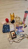Full overview of the lot showing all items on floor including tarot deck, Buddha figurine, angels, keychains, necklaces, box contents and multiple decorative items