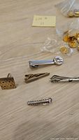 Photo showing several tie clips in silver and gold tones with different designs on wood surface.