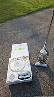 iRobot Roomba robotic vacuum in foam packaging next to upright Shark stick vacuum on pavement