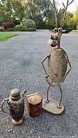 Photo showing the full lot of three items together on pavement, slender metal reindeer figure, tea tin and coffee pot
