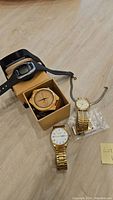 Four watches including one wooden watch in box, two gold-tone analog watches, and one black digital watch.